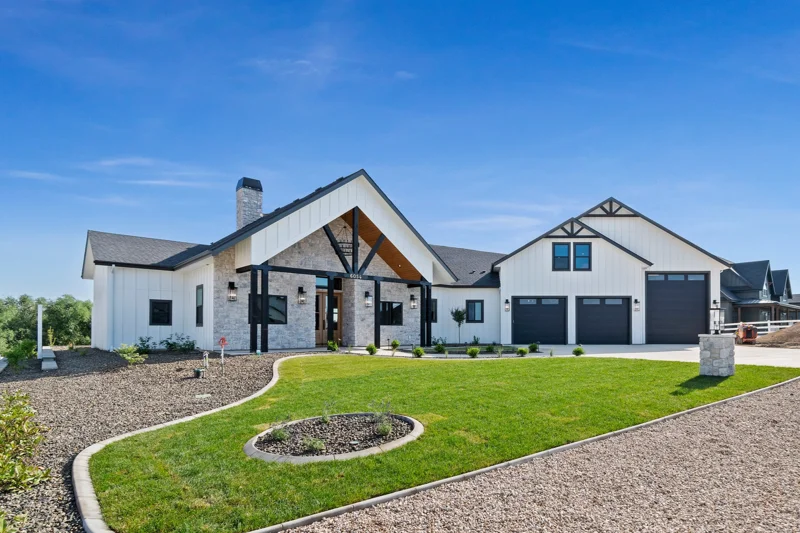 Modern white house in Weatherby Estates with black garage doors, stone accents, and a landscaped lawn under a blue sky.