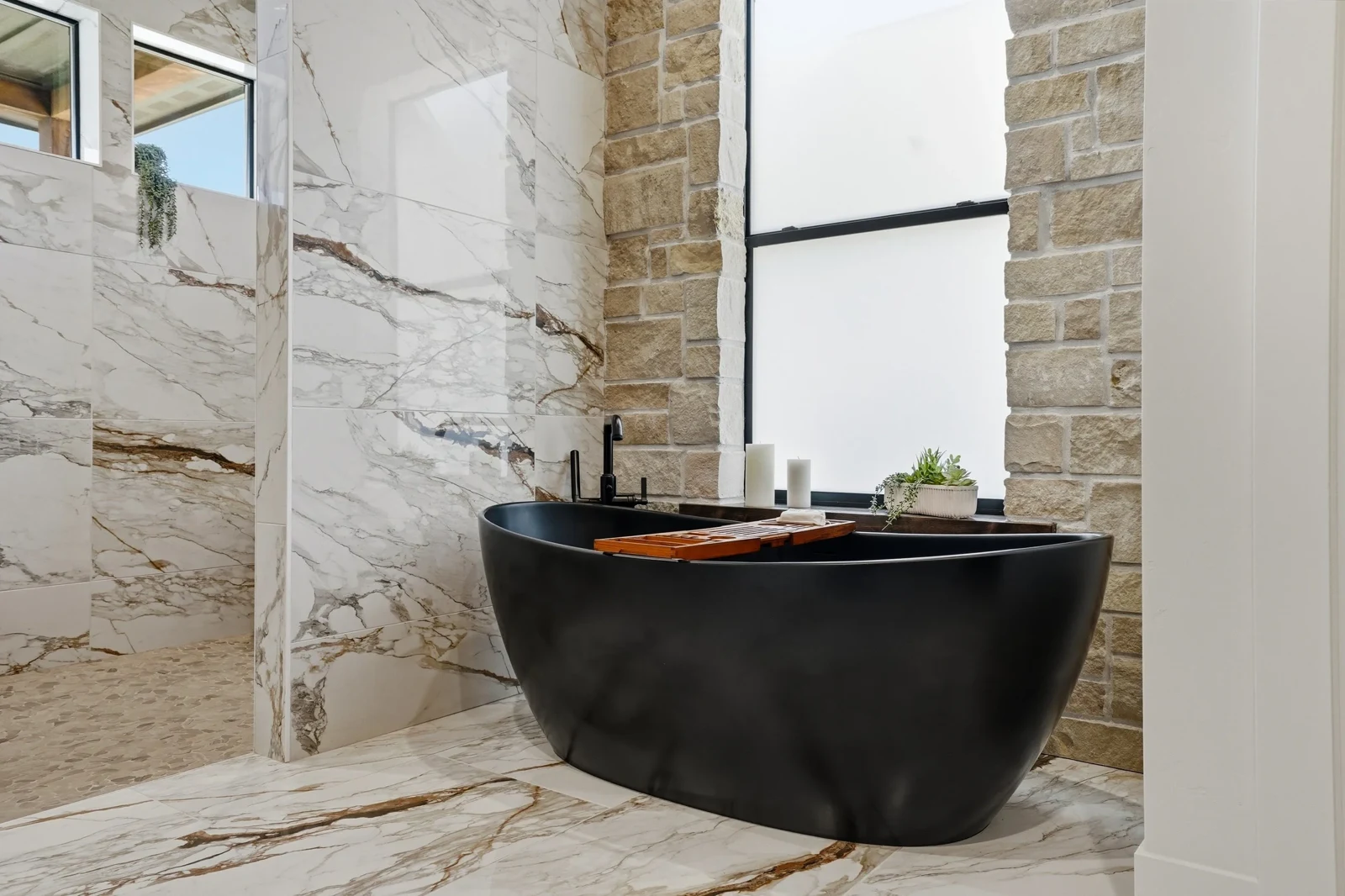 Black freestanding bath within a stone-walled bathroom